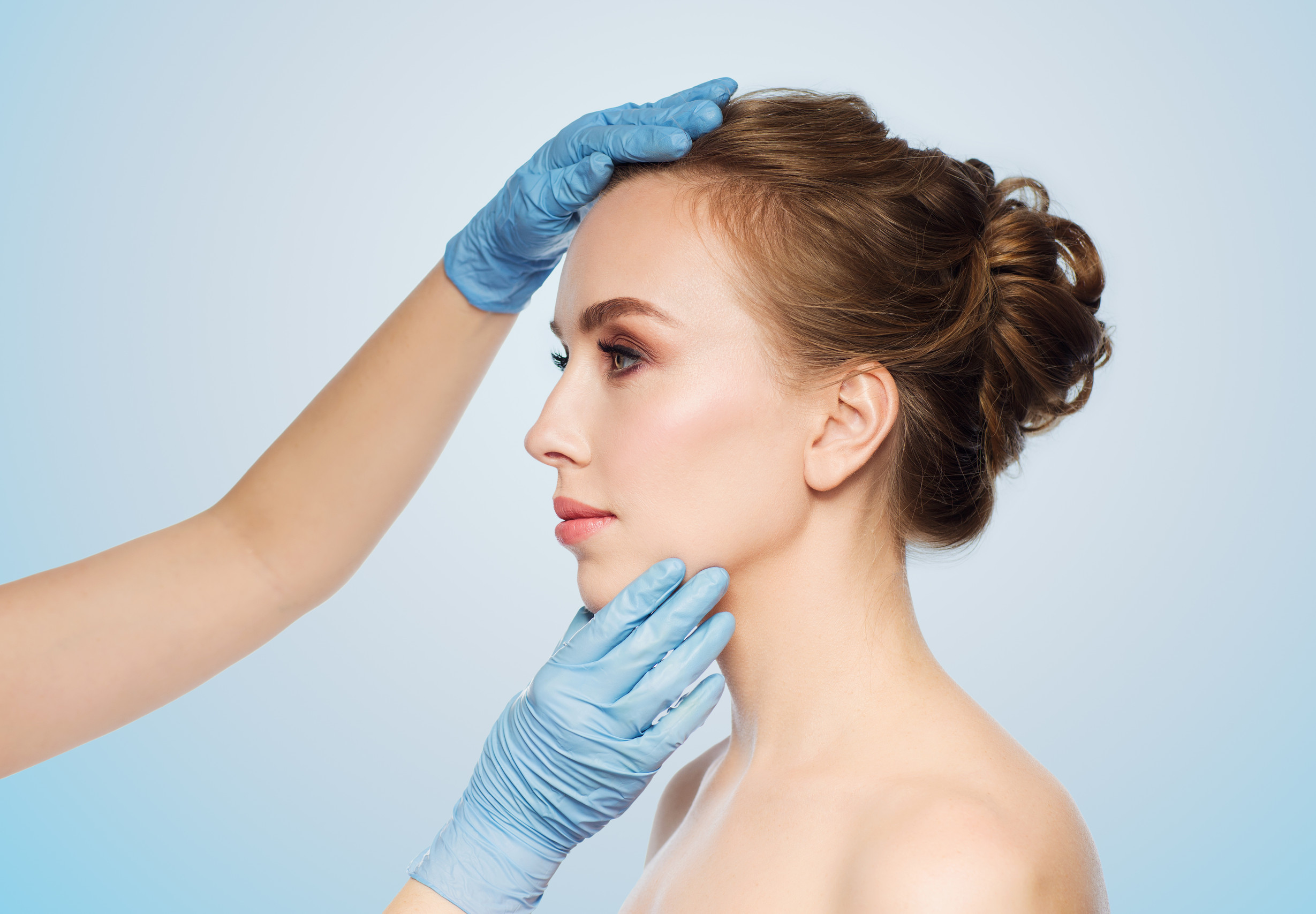 surgeon or beautician hands touching woman face people, cosmetology, plastic surgery and beauty concept - surgeon or beautician hands touching woman face over blue background